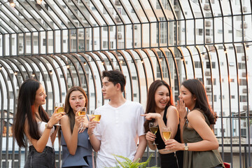 Group of happy Asian girls and man celebrating party, dancing and drink at rooftop in sunset together, female gang and boy friend having fun, chatting, laughing, night lifestyle of young people