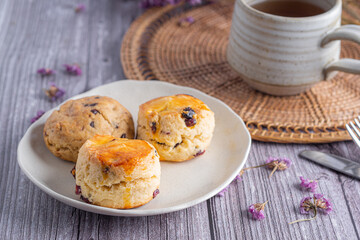 Traditional British scones on a plate with a teacup on a wooden table with a purple flower blurred background