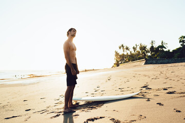 Shirtless male surfer stretching neck on beach