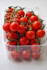 Fresh, red cherry tomatoes with green stems isolated on white background in retail packaging.