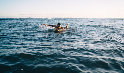 Shirtless young sportsman floating on surfboard