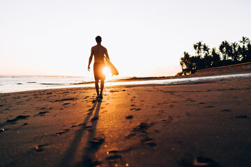 Rear view of sportive man walking at summer seashore with sunset spending day for practice hobby...