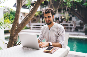 Young male entrepreneur working on laptop and looking at camera