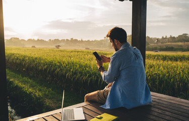 Anonymous guy messaging on smartphone during sunset in countryside