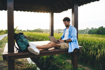 Happy young man resting in meadow gazebo with netbook