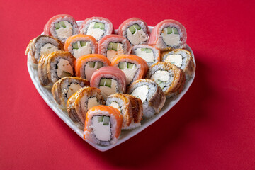 Sushi set of salmon, tuna and eel with philadelphia cheese in plate as heart on red background. Valentine day food concept.