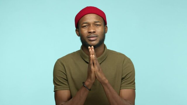 Slow motion of Black man 20s years with beard and red beanie, asking for favour, say please and begging help, need something, standing over blue background