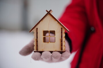 Close up of woman's hand in glove holding small wooden house in wintertime. Concept of purchasing...