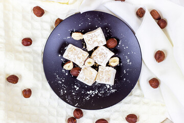 Top view of traditional Turkish delight sweet homemade rahat lokum with hazelnuts and sugar powder on black plate.