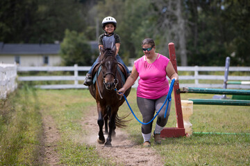 child riding a pony with an instructor