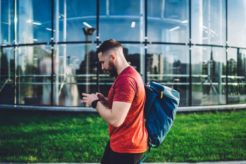 Focused man with backpack walking near modern glass building