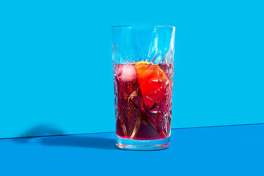 Vaso de cristal con cocktail vermut proyectando sombra sobre un fondo azul liso y aislado. Vista de frente. Copy space