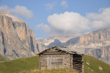 Drewniana, pasterska chata w Dolomitach na tle górskich szczytów - obrazy, fototapety, plakaty