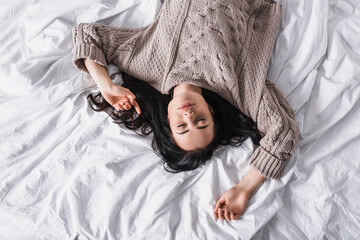 top view of brunette woman in sweater sleeping in bed at morning
