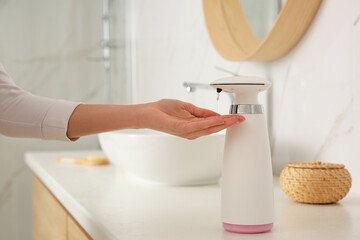 Woman using automatic soap dispenser in bathroom, closeup