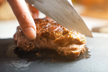 Woman cutting fried duck fillet with a knife.