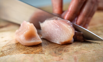 Woman is cutting chicken fillet with a knife.