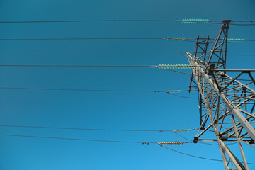 High voltage tower against blue sky on sunny day, low angle view
