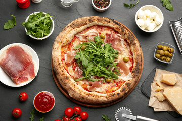 Tasty pizza with meat and arugula on black table, flat lay