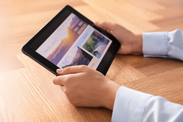 Woman booking tickets online on tablet at wooden table, closeup. Travel agency concept