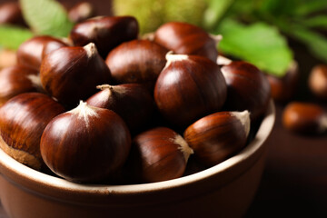 Fresh sweet edible chestnuts in bowl on table, closeup
