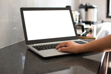 Closeup, A woman's hand is typing on a laptop keyboard to search out how to cook. notebook computer white screen on the table. Has a pot on the gas stove. Blurred background, moke up, clipping path