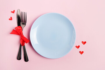 Festive table setting for Valentines Day with blue empty plate on pink table with red hearts