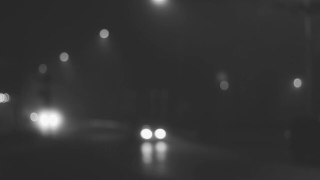 Black and white 4k video of defocused blurry night rainy city road with moving cars in darkness.