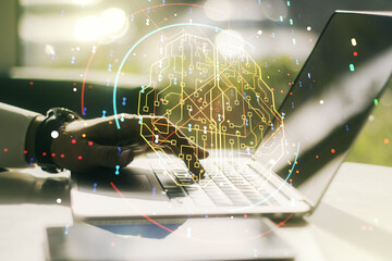 Double exposure of creative artificial Intelligence symbol with hands typing on laptop on background. Neural networks and machine learning concept