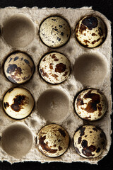 Quail eggs in the cardboard packing on the grey scratched table.