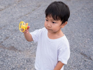 Asian child boy playing a flying spinner toy outdoor with cute face. Concept of freedom, family...