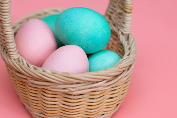 Fototapeta na wymiar Easter decor: colored eggs in a basket, pink background, pastel colors, close-up. Preparing for Easter. The photo