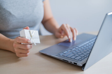 Faceless woman holding gift box and typing on laptop.