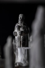 Fototapeta na wymiar A black and white portrait of a stone sculpture of a king on a chess board in between other chess pieces. It is the most important piece in this strategic duel.