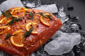 salmon fillet with orange slices on pieces of ice on a black background