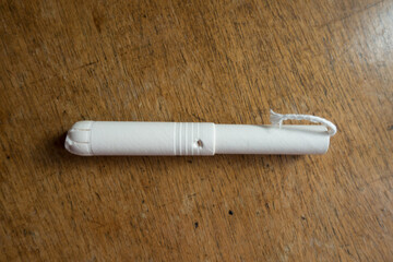 One tampon with cardboard applicator on wooden table from above