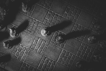 A top down portrait of the beginning of a match of chess. The chessboard and the pieces are made of stone and represent sculptures. The first move has been made in the strategic duel of armies.