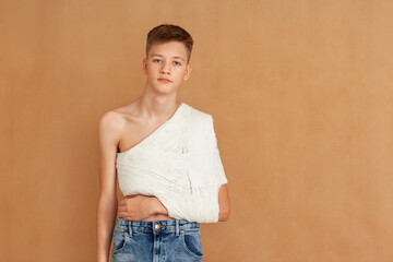 Yuong boy on a beige isolated background with a back, collarbone or shoulder injury. Medical care...