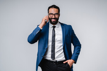 Confident young Arab businessman talking on mobile phone isolated over grey background