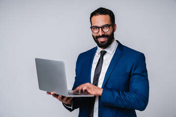 Happy cheerful young islamic businessman in formal clothing using laptop isolated over grey background