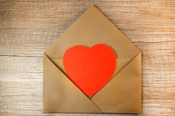 On the wooden surface is an open envelope with a red heart inside.