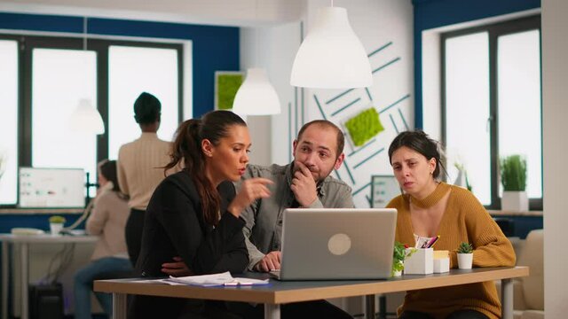 Business young people discussing new project, working on stratup report using laptop sitting together at desk in modern company offine. Teamwork, friendly good work relation, cooperation concept