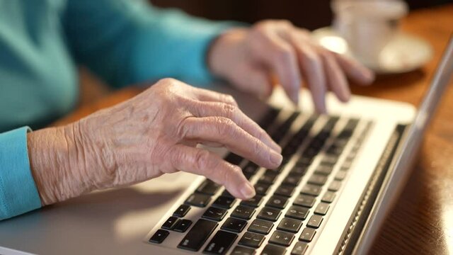 Extreme closeup of elderly womans arthritis hands while she types on laptop computer keyboard.