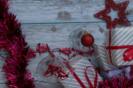 two martini glasses surrounded by new year gifts with red christmas decorations on a blue wooden table. High quality photo