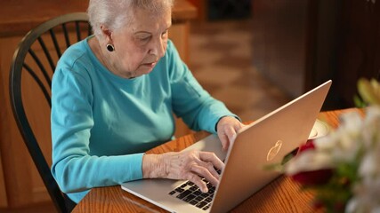Overhead view of elderly woman sitting at dining room table and working on laptop computer with tea. - Powered by Adobe
