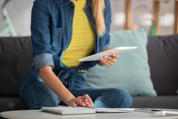 Cropped view of woman with digital tablet sitting near notebook at home on blurred background