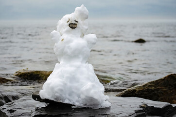 A real handmade snowman on a rock by the sea