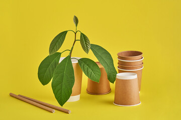 Drinking tubes made of paper and cornstarch, biodegradable material and eco paper glasses with green sprout leaves on yellow trend color 2021 background. Zero waste and plastic free concept. Top view.