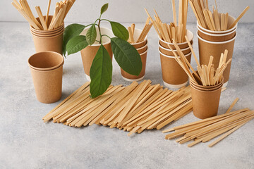 Wooden Drink Stirrers and eco paper glasses with green sprout leaves on grey background. Zero waste...