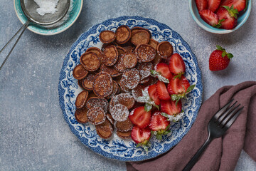 Mini chocolate pancake cereal with strawberries for breakfast on gray concrete table. Trendy home breakfast with tiny pancakes. Top view.